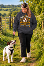 A woman walking a dog on a grassy path outdoors, wearing a dark gray hoodie with a 'Dog Sister Chief Best Friend' graphic print. The hoodie features a cartoon dog face and decorative text in gold and white.