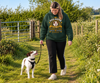 A woman walking a white and brown dog on a grassy path wearing a dark green hoodie with a 'Dog Sister' graphic print, black pants, and white Croc shoes.