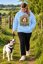 A woman walking a small white and brown dog on a grassy path outdoors, wearing a light blue hoodie with a large 'Dog Sister' graphic print on the front.