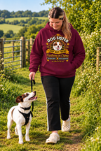 A woman walking a Jack Russell Terrier on a grassy path outdoors, wearing a maroon hoodie with a 'Dog Sister' graphic print and black pants.