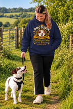 A woman walking a white and brown dog on a grassy outdoor path wearing a navy blue hoodie with a 'Dog Sister' graphic print, black pants, and white clogs.