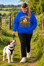 A woman walking a white and brown dog on a grassy outdoor path, wearing a bright blue hoodie with a large graphic print that reads 'DOG SISTER CHIEF BEST FRIEND The Power of Love' and black pants.