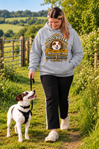 A woman walking a white and brown dog on a grassy path outdoors, wearing a light gray hoodie with a 'Dog Sister' graphic print. The hoodie features a cartoon dog face and text that reads 'Dog Sister Chief Best Friend' and 'Pup Parent & Owner'.