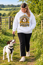 A woman walking a white and brown dog on a grassy outdoor path, wearing a white hoodie with a 'Dogsister' graphic print and black pants.