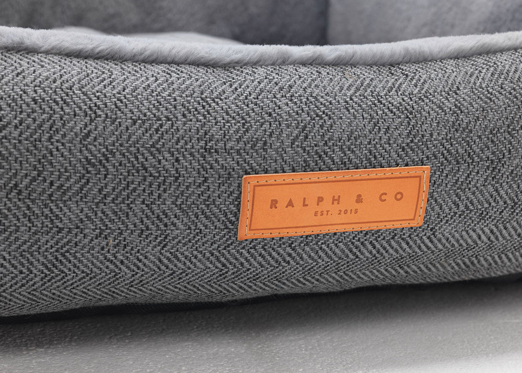 Gray textured pet bed with a brown leather label reading 'Ralph & Co' on a gray background.