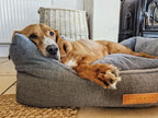 Dog lying on a textured gray pet bed with a visible brand logo.
