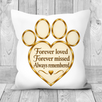 A square white throw pillow with a printed gold and beige paw print and heart design, featuring the text 'Forever loved Forever missed Always remembered' on a rustic gray wood plank background.