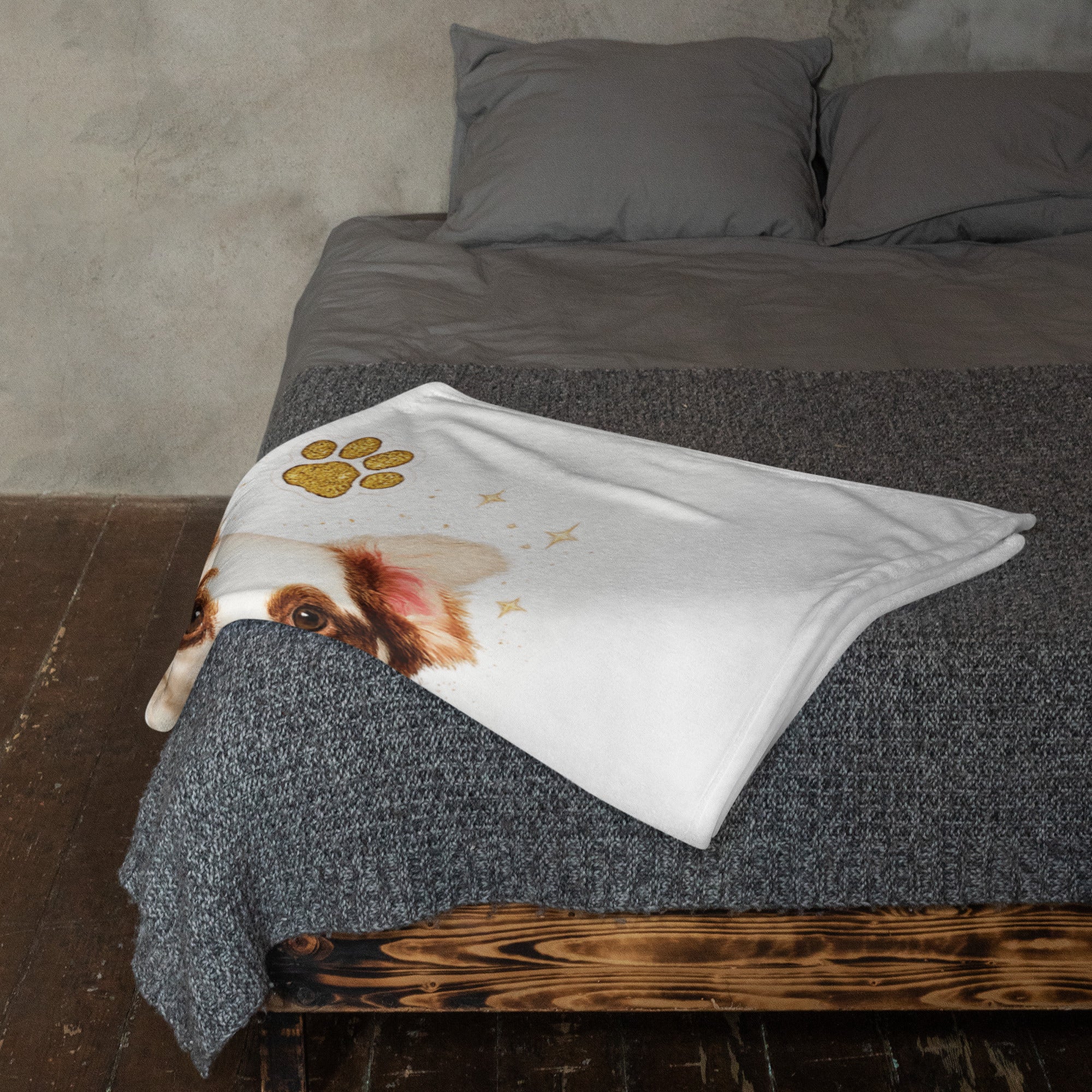 A white pet blanket featuring a printed dog face and gold paw prints, draped over a bed with gray bedding.