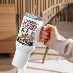 A white insulated tumbler with a clear lid and straw is held by a person's hand in a warm indoor setting. The tumbler